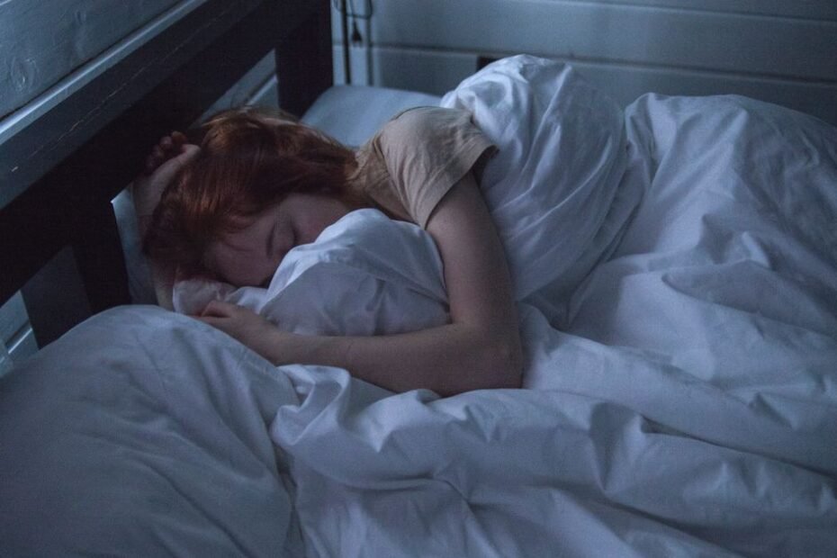 Woman sleeping peacefully in a dark, calm bedroom that supports healthy sleep hygiene
