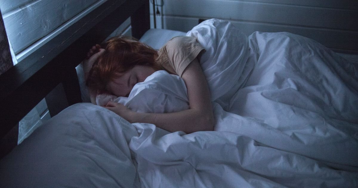 Woman sleeping peacefully in a dark, calm bedroom that supports healthy sleep hygiene